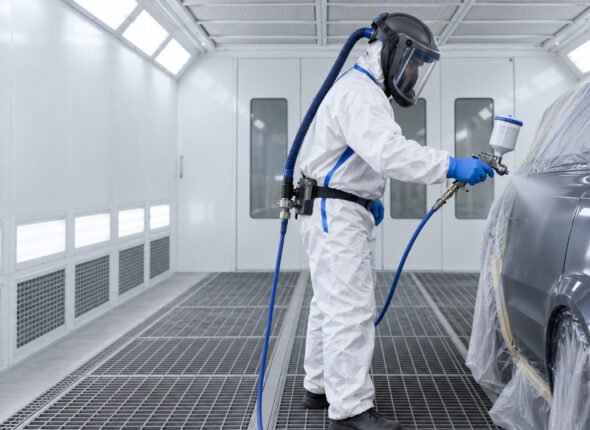 Worker spraying safely in a ventilated booth while wearing air-fed breathing apparatus and protective clothing