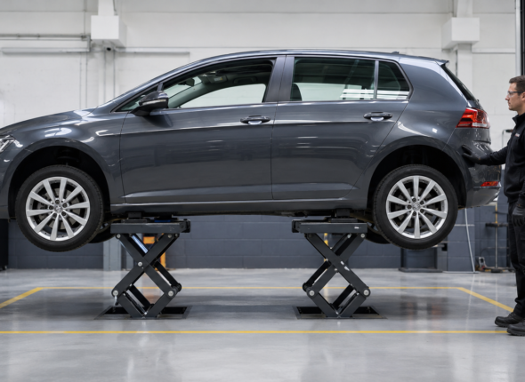 Vehicle technician checking a car securely raised on a short-platform scissor lift in a professional workshop